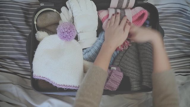 top view of a girl who prepares the suitcase to go to the mountains with hat, earmuffs, gloves, sweater and sunglasses