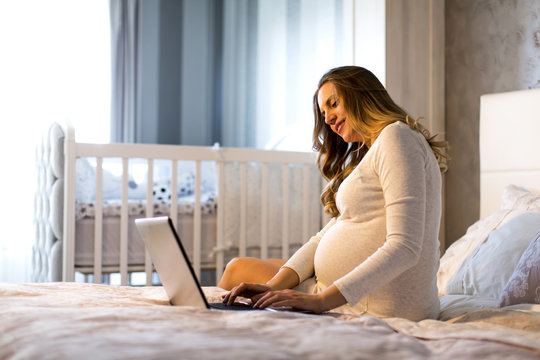Young pregnant woman with laptop in the bed