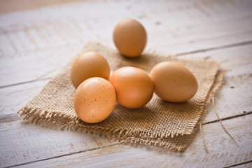 Fresh brown eggs on burlap cloth on white plank wood background, Easter, simplicity, cleaness, minimalistic style, rural still life