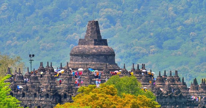 tourists in colorful clothes with umbrellas visiting beautiful ancient Buddhist landmark Borobudur temple in Java Indonesia