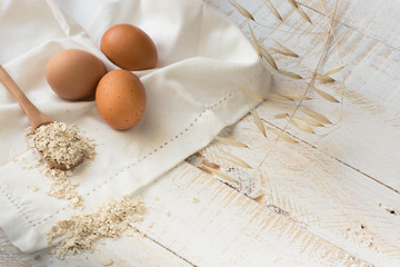 Fresh organic eggs,dry oatmeal flakes on wooden spoon scattered over white linen cloth, wood background, healthy ingredients, mindful eating,beauty, skin care