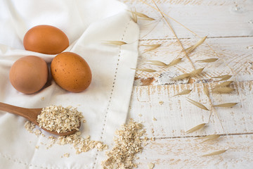Brown eggs,dry oatmeal flakes on wooden spoon scattered over white linen cloth, wood background, healthy ingredients, mindful eating,beauty, skin care concept