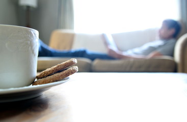 Tea and biscuits or cookies on a wooden coffee table, man relaxi