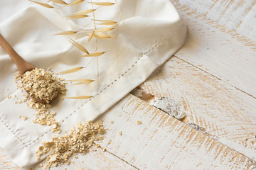 Dry oatmeal flakes on a wooen spoon over a white linen cloth, plant twig, plank wood background, clean eating, rustic, health concept, beauty, skin care, top view