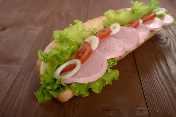 sandwich with sausage and vegetables on a wooden table