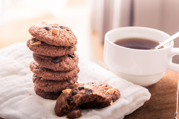 Chocolate chip cookies on napkin and hot tea on wooden table.