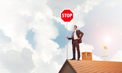 Caucasian businessman on brick house roof showing stop road sign