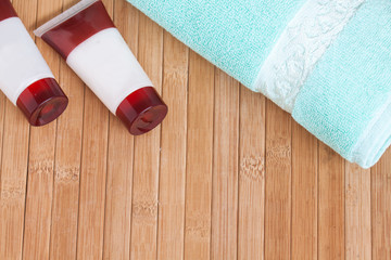 Obraz na płótnie Canvas Lotion or shampoo tubes and bath towel on wooden mat. Spa and beauty saloon motif wallpaper