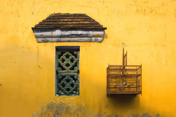 Aged yellow wall with small window and bird cage
