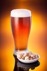 light beer in frosty glass with pistachios over bright amber bac