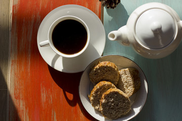 A hot morning coffee served in a beautiful cutlery with delicious brown bread on an orange and light cyan old wooden table.
