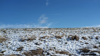 Partially snow covered hill and blue sky with some clouds