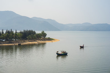 Fototapeta na wymiar River scene in Vietnam, with fishing boat, strip of land and mountain on background