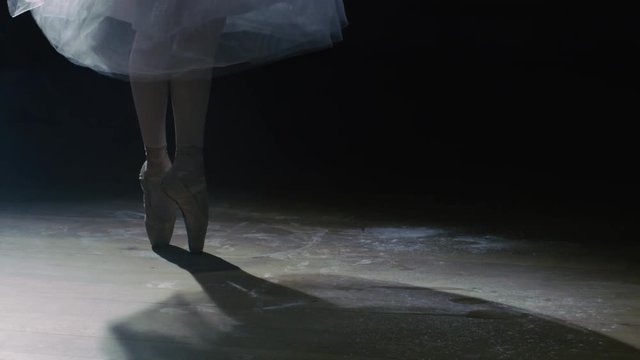 Close-up Shot of Ballerina's Legs. She's Dancing and Spinning on Her Pointe Ballet Shoes in the Spotlight with Darkness Around. In Slow Motion. Shot on RED EPIC-W 8K Helium Cinema Camera.