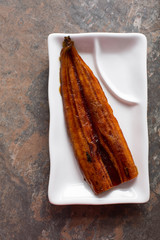 Japanese roasted eel on a white rectangular plate. 