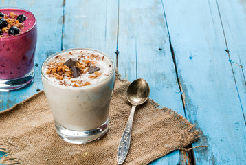 Easy and light healthy breakfast of yogurt, fruit smoothies, granola and dark chocolate, on blue...