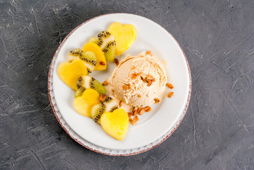 Romantic foods for Valentine's Day. Fruit salad with ice cream ball on a plate, top view. Fruits cut in the shape of hearts, copy space