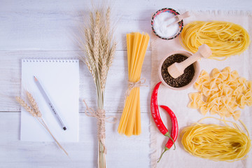 Pasta and wheat spikelets on a white wooden background
