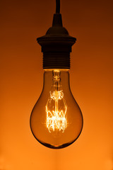lighted vintage incandescent bulb on orange background