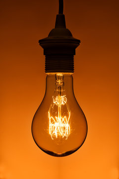 lighted vintage incandescent bulb on orange background