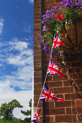 British flags are hanging on a rope. Brick wall. Flowers in pots.