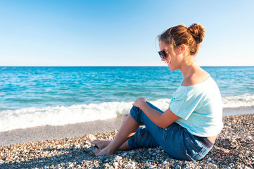 Fototapeta na wymiar Young beautiful teenage girl sitting on Mediterranean Sea pebble