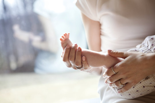 Cropped image of woman carrying baby girl by window at home