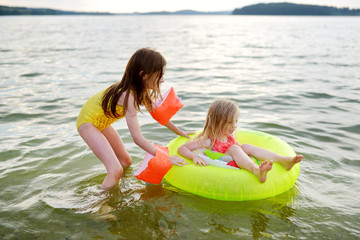 Little sisters having fun swimming in a lake using inflatable rubber