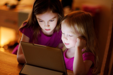 Two adorable little sisters playing with a digital tablet