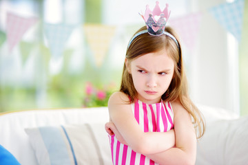 Moody little girl wearing princess tiara feeling angry and unsatisfied