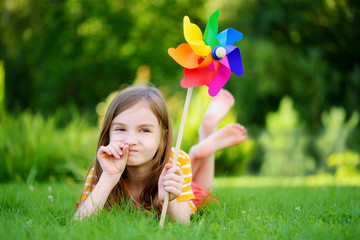 Adorable little girl holding colorful toy pinwheel on sunny summer day