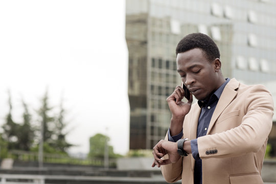 Businessman checking the time while using smart phone in city