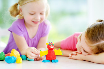Obraz na płótnie Canvas Two cute little sisters having fun together with colorful modeling clay at a daycare