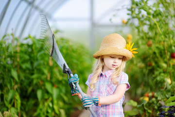 Adorable little girl wearing straw hat holding garden tools