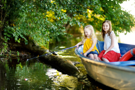 Two cute little girls having fun in a boat by a river at beautiful summer evening