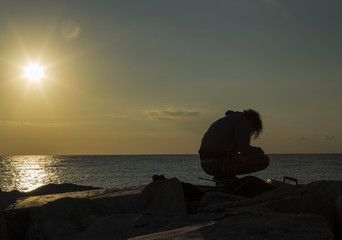 Naklejka na ściany i meble Man fishing in first rays of sunlight on sea shore