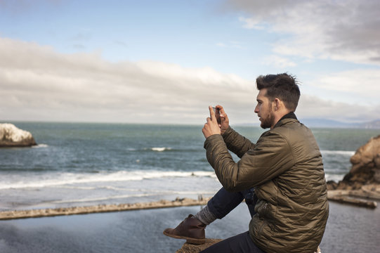 Side view of man taking picture of sea through smartphone