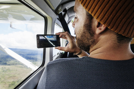 Rear view of man taking photograph through smartphone from airplane window