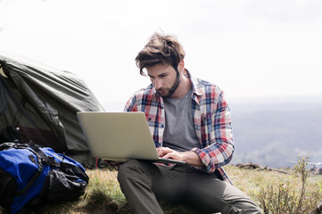 Man using a laptop while sitting on hill 