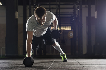 Man doing push ups while lifting dumbbells in gym