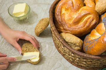 Woman spread the butter on the slice of bread and different bread in the wicker basket