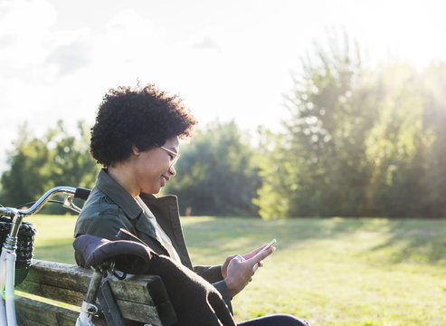 Smiling woman using smartphone while sitting on bench at park