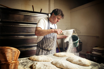 Male baker sprinkling flour on bread dough at bakery