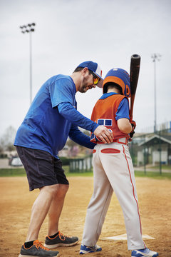 Coach assisting boy in playing baseball on field
