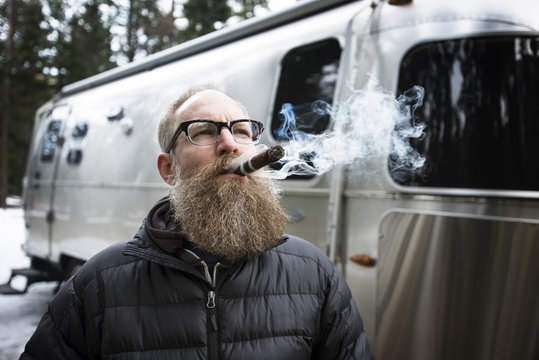 Thoughtful man smoking cigar outside campervan in forest