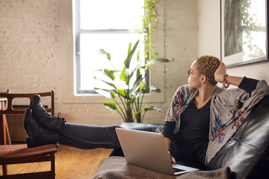 Thoughtful Woman Looking Away While Using Laptop On Sofa At Home