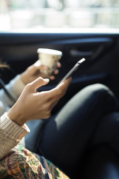 Cropped image of woman using smart phone while holding disposable glass in taxi