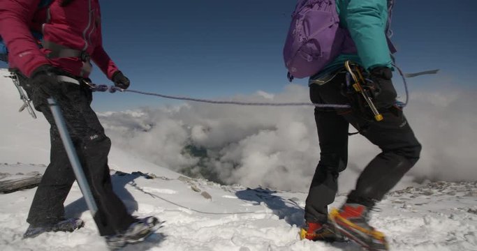 Two Mountaineers Roped Together for Safety Cross Mountains Above the Clouds.