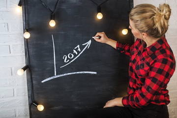 An attractive young woman with chalk at the blackboard. Graph of growth or success.