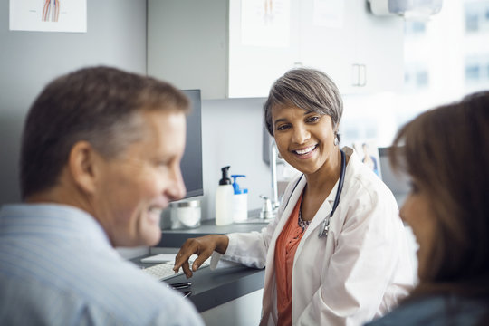 Happy Female Doctor Looking At Patient In Clinic